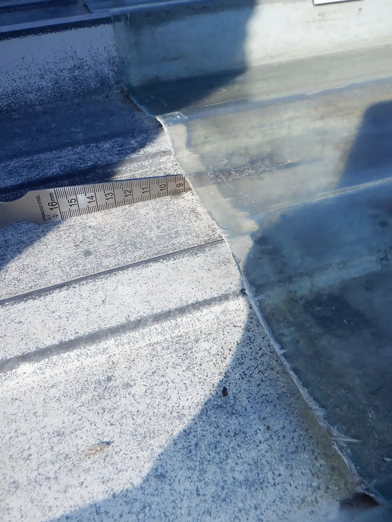 Mesure d’un écart entre deux plaques de toiture en fibrociment à l’aide d’un réglet métallique.