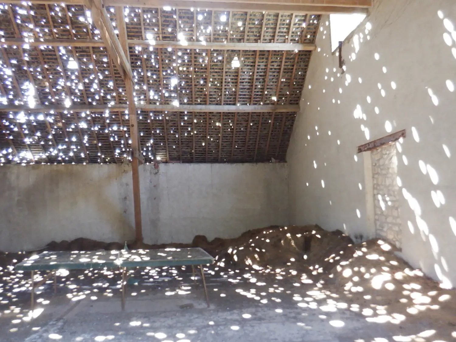 Charpente de grange laissant passer la lumière à travers de nombreuses tuiles manquantes ou cassées.