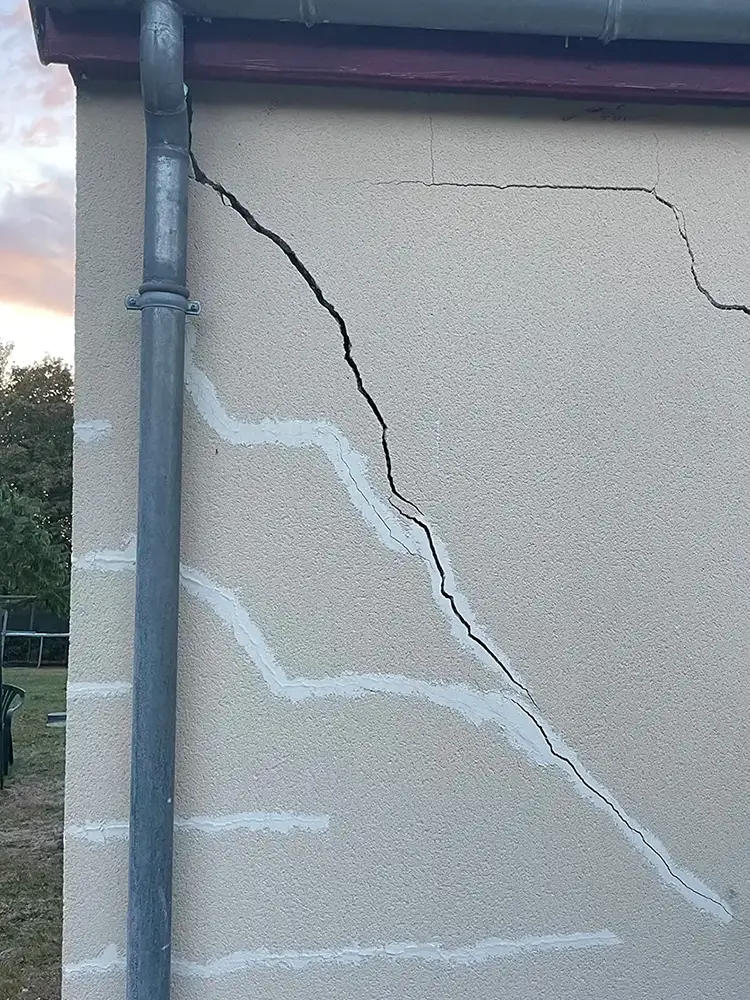Fissure en escalier importante sur façade d’une maison entre une fenêtre et un angle de mur.