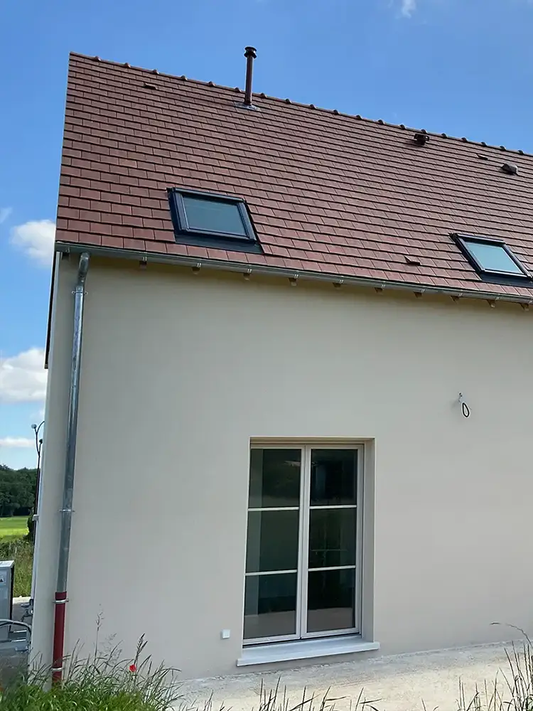 Façade latérale d’une maison neuve avec toiture en tuiles, fenêtres de toit et baie vitrée