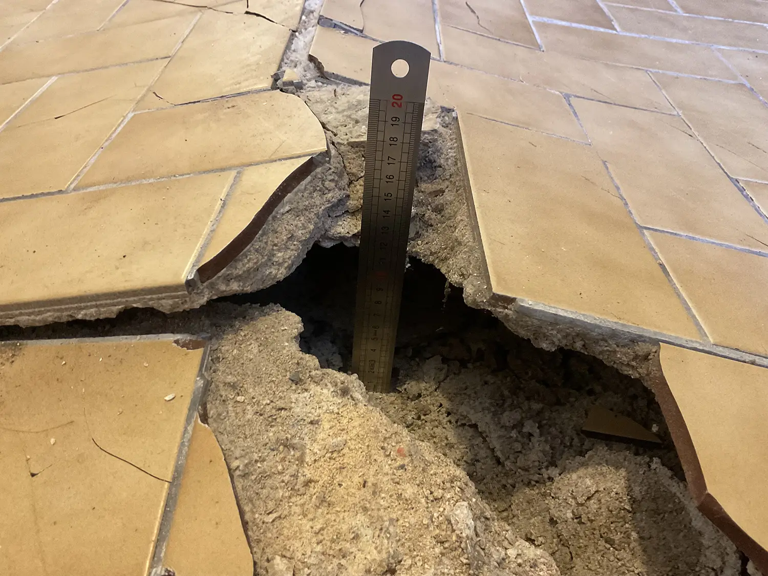 Trou sous carrelage soulevé avec réglette indiquant la profondeur dans une dalle endommagée.