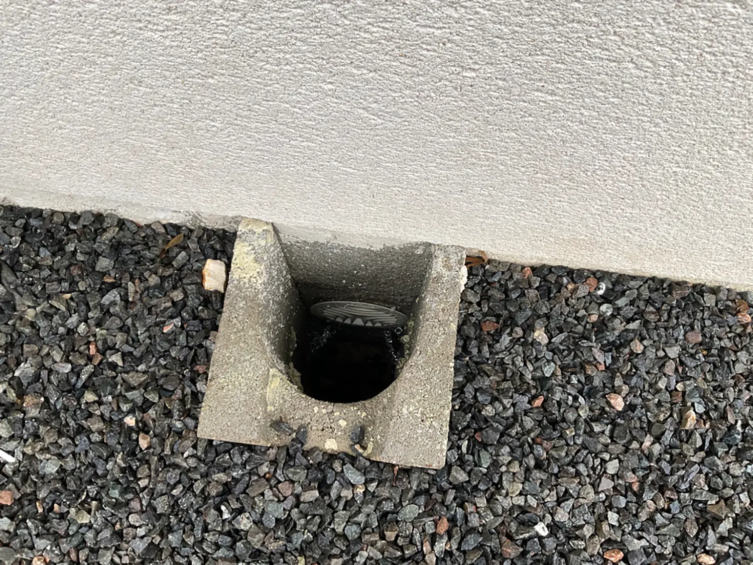Regard de drainage extérieur en béton au pied d’un mur