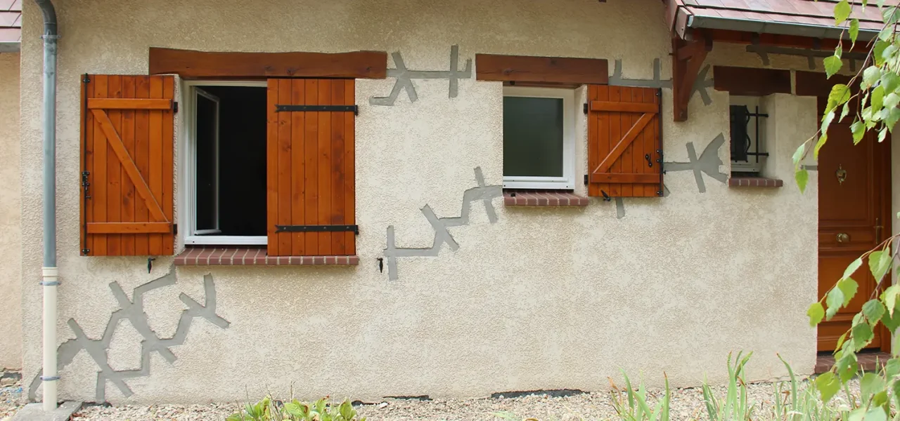 Façade d'une maison avec reprises en sous-œuvre visibles sur l'enduit.