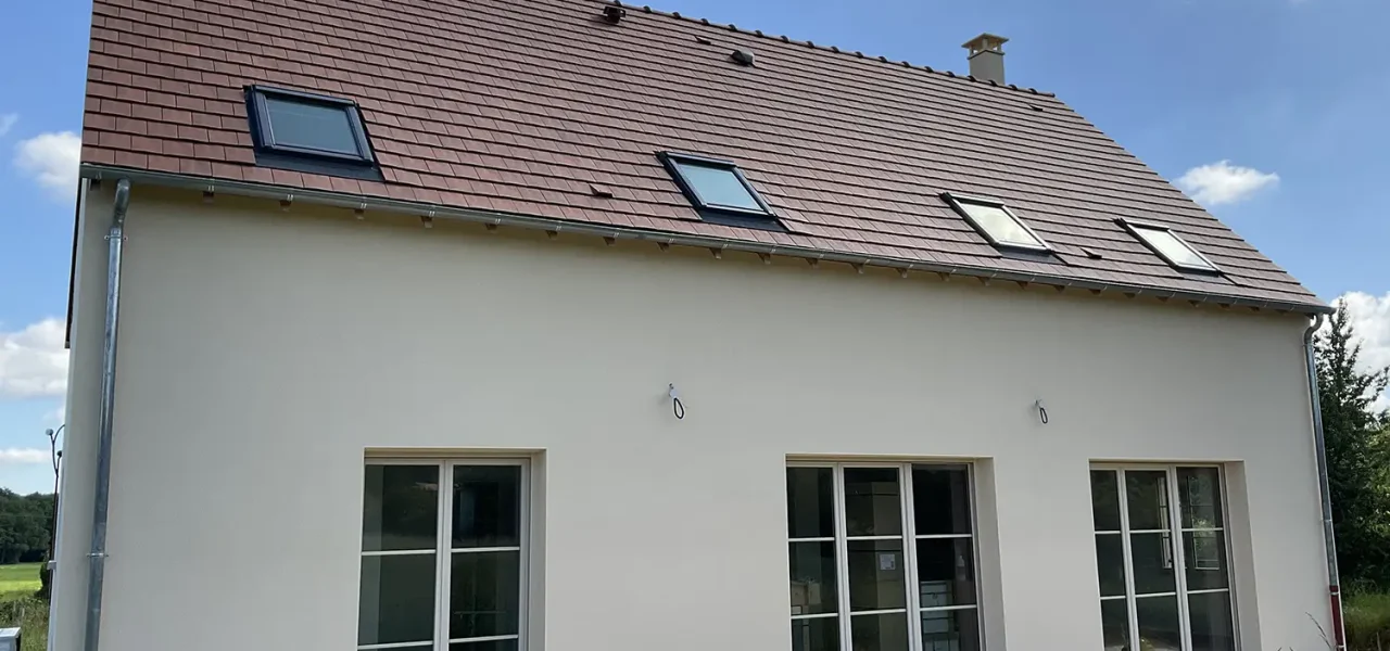 Façade arrière d'une maison contemporaine avec toiture à deux pans, fenêtres en aluminium et enduit beige clair