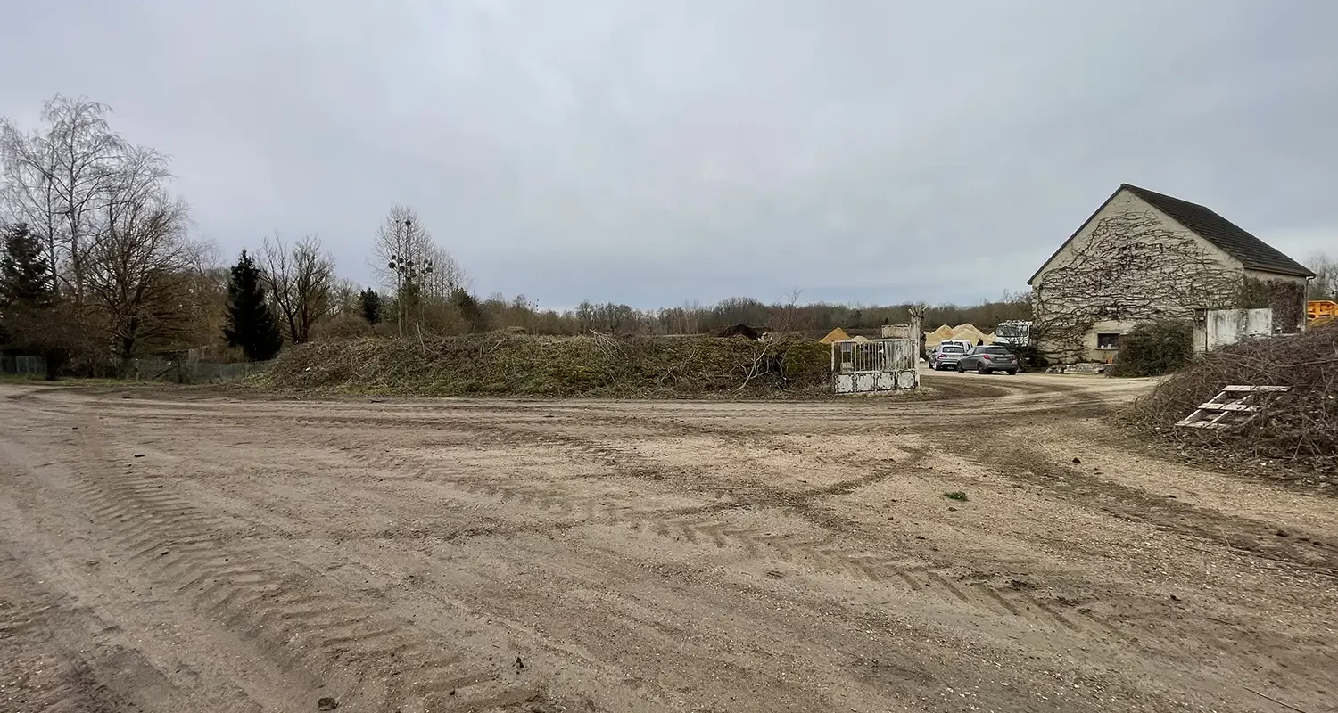 Terrain nu en friche avec bâtiment en pierre et véhicules stationnés